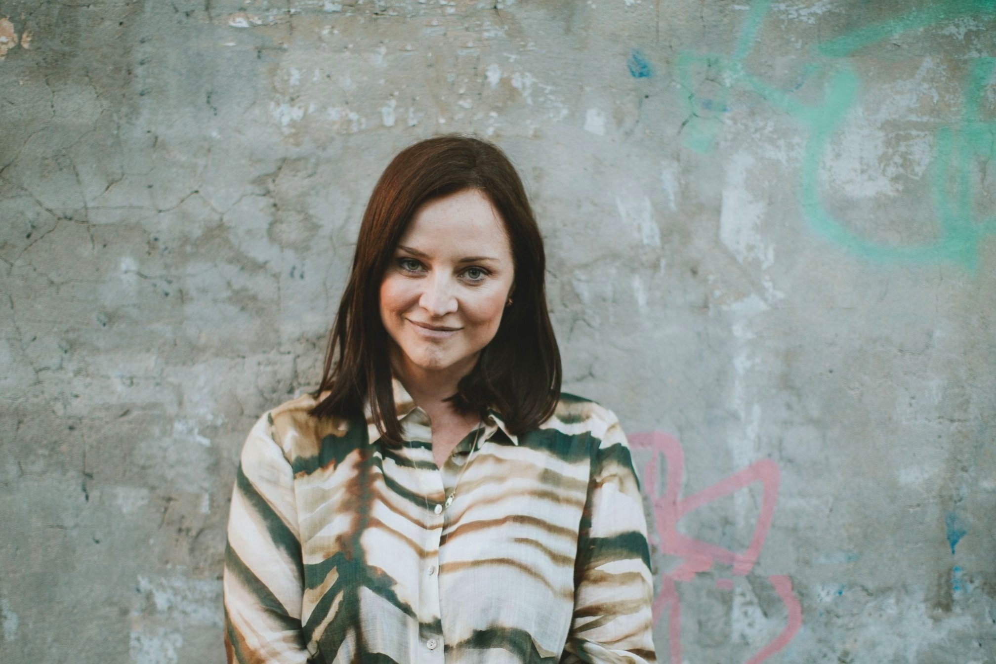 Alexandra Carlton in an olive striped shirt against a painted concrete wall